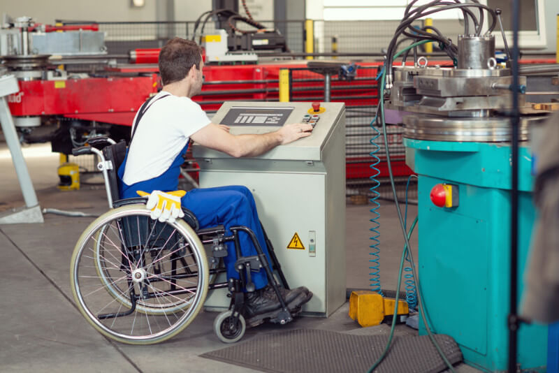 A young man in a wheelchair working in a machine factory.