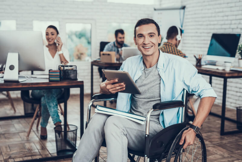 A smiling young Latino man sitting in a wheelchair and working in a design studio.