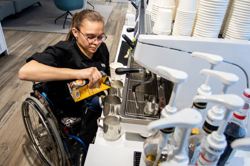 Young disabled woman in a wheelchair working as a barista, making an espresso.