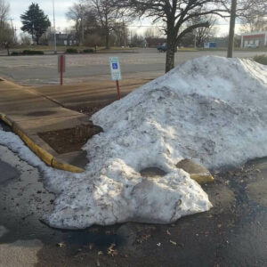 A pile of snow that has been plowed into an accessible parking space.